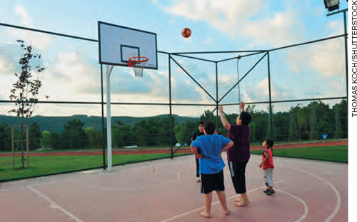 IMAGEM: três crianças arremessam um bola de basquete em direção à cesta, em uma quadra esportiva. FIM DA IMAGEM.