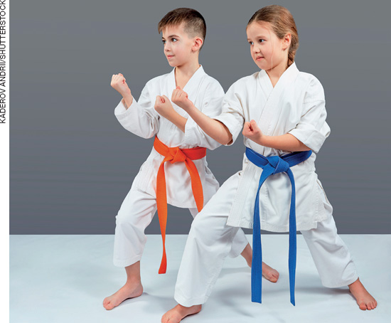 IMAGEM: um menino e uma menina usam quimonos e fazem o mesmo movimento de luta kung fu, com uma das pernas flexionadas e os punhos cerrados em posição de defesa. ele usa uma faixa laranja e ela, uma faixa azul. FIM DA IMAGEM.