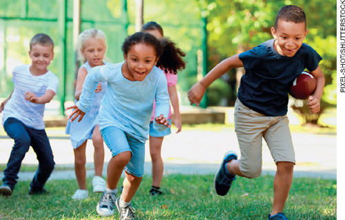 IMAGEM: cinco crianças sorriem e correm em um gramado. um dos meninos segura uma bola de futebol americano debaixo do braço. FIM DA IMAGEM.