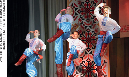 IMAGEM: quatro garotos fazem uma coreografia, com uma das pernas levantada e flexionada. eles usam uma camisa bordada, calças largas e botas de couro de cano alto. FIM DA IMAGEM.