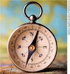 IMAGEM: fotografia de uma bússola, semelhante a um relógio de bolso. ela é circular, tem um ponteiro que passa pelo centro, os pontos cardeais e colaterais, e numeração ao redor dos pontos. FIM DA IMAGEM.