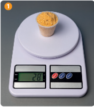 IMAGEM: um copo cheio de farinha de milho está sobre uma balança digital. o peso indicado no visor é de 28 gramas. FIM DA IMAGEM.