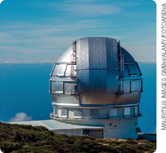 IMAGEM: um grande telescópio coberto por uma estrutura metálica de formato arredondado em uma área ao ar livre. FIM DA IMAGEM.