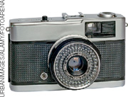 IMAGEM: máquina fotográfica antiga. é um pouco menor do que suas antecessoras e a estrutura que contém a lente é projetada para frente por uma peça sanfonada. FIM DA IMAGEM.