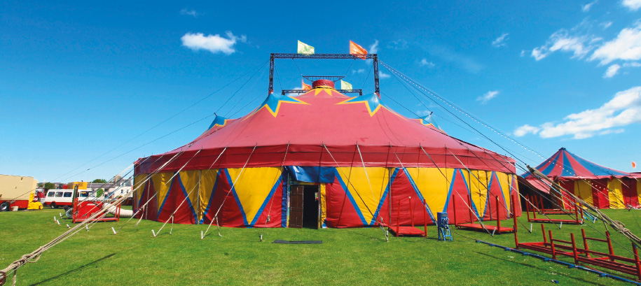 Imagem: Fotografia. Tenda de circo vermelha com triângulos amarelos em volta e no topo há estrelas azuis.  Fim da imagem.