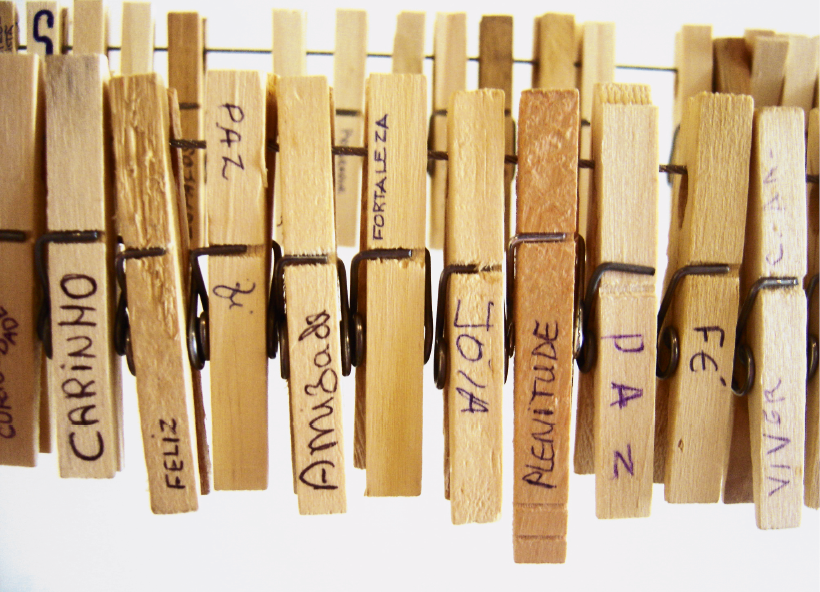 Imagem: Fotografia. Pregadores de madeira pendurados em um varal e com palavras escritas na base: carinho, feliz, paz, fé, amizade, fortaleza, joia, plenitude, paz, fé e viver.  Fim da imagem.