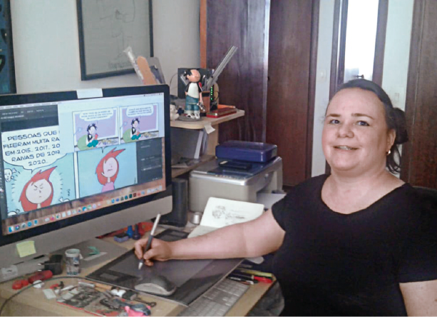 Imagem: Fotografia. Chantal, mulher com cabelo liso e preso, olhos escuros, nariz grande e lábios finos está sentada e segurando uma caneta sobre uma mesa digitalizadora. Na frente dela há um monitor grande com desenhos de personagens e fala. Ao lado, uma impressora, vários lápis e canetas sobre uma mesa. Fim da imagem.