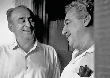 Imagem: Fotografia em preto e branco. À esquerda. Carybé está sorrindo. À direita, Jorge, homem com cabelo encaracolado e curto, sobrancelhas e bigode grossos e nariz grande está sorrindo. Fim da imagem.