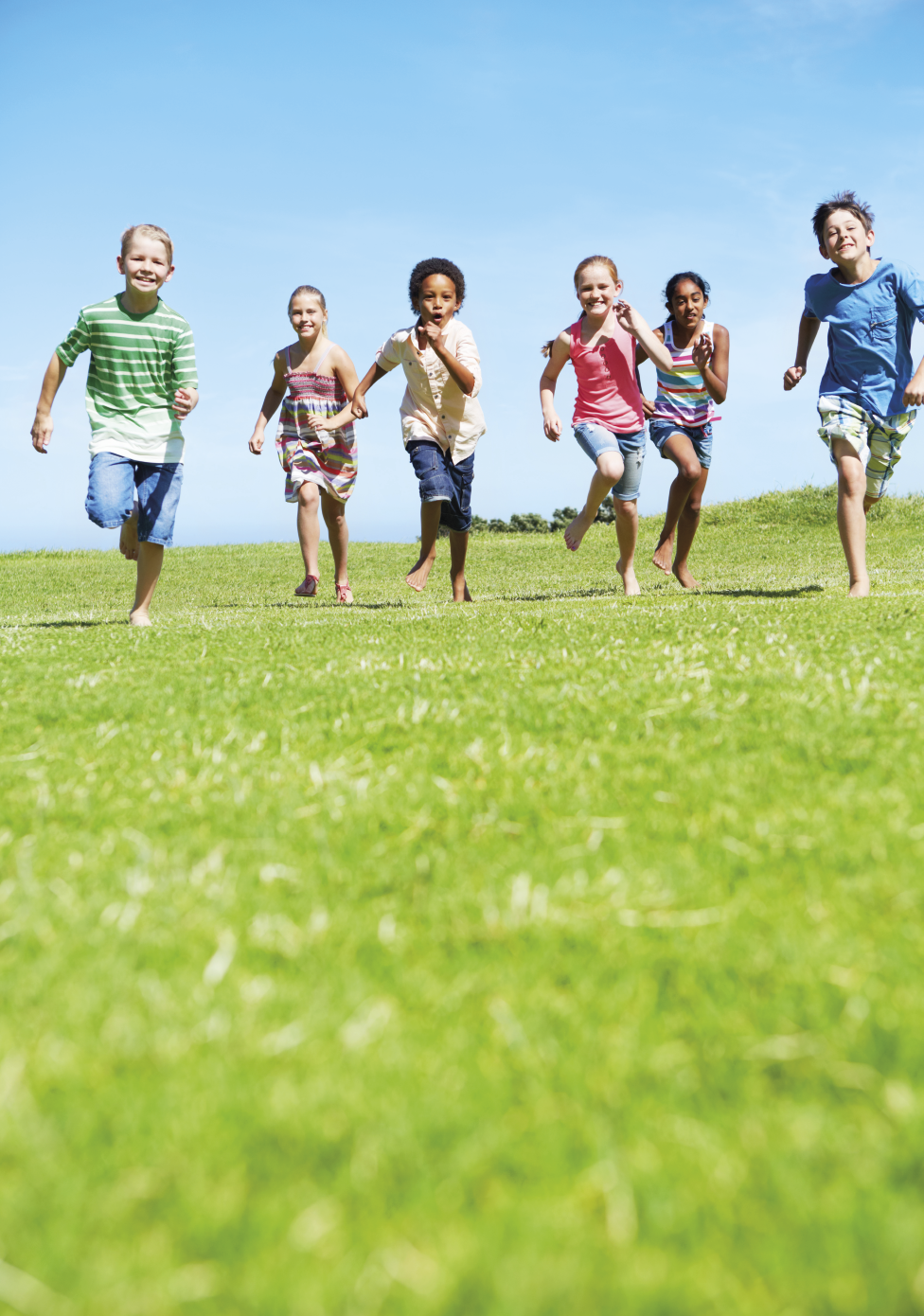 Imagem: Fotografia. Crianças diversas, sendo três meninos e três meninas com roupas coloridas. Estão correndo em um gramado em direção à câmera. Fim da imagem.