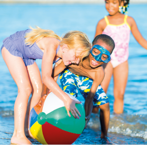 Imagem: Fotografia. Três crianças na beira do mar brincando com uma bola grande colorida. Fim da imagem.