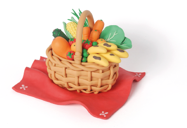 Imagem: Fotografia. Cesto de vime marrom com frutas e legumes. Está sobre uma toalha vermelha. Fim da imagem.