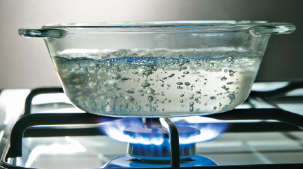 Imagem: Fotografia. Recipiente transparente com água fervente ao fogo. Fim da imagem.