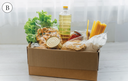 Imagem: Fotografia. B. Caixa de papelão cheia de alimentos diversos: Alface, rosquinha, óleo, molho, sementes, lata, macarrão e açúcar. Fim da imagem.