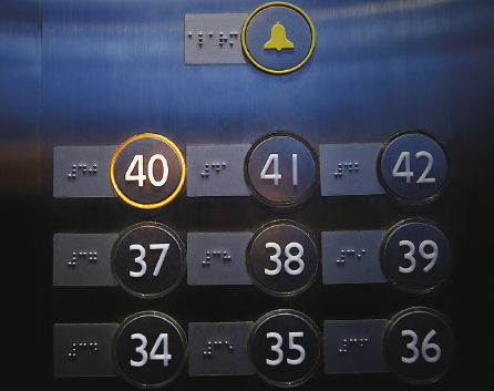 Imagem: Fotografia. Botões de um elevador com números em braile. Fim da imagem.