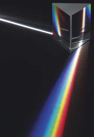 Imagem: Ilustração. Prisma recebendo luz branca e liberando luz branca decomposta colorida. Fim da imagem.