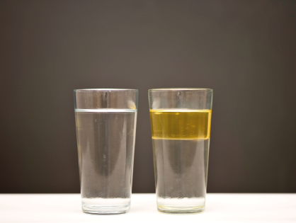 Imagem: Fotografia. Dois copos de vidro com líquidos. À esquerda, líquido transparente. À direita, divisão de líquido transparente na parte inferior e líquido translucido em amarelo na parte superior. Fim da imagem.