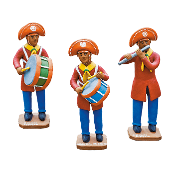 Imagem: Fotografia. Esculturas de homens de chapéu em forma de meia lua, vestindo camiseta laranja e calça azul. Estão tocando instrumentos musicais. Fim da imagem.