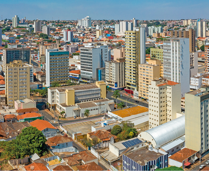 Imagem: Fotografia. Vista aérea de cidade coberta por casas e prédios. Fim da imagem.