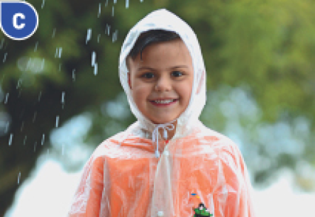 Imagem: Fotografia C. Um menino com capa de chuva transparente e capuz está sorrindo. Em volta dele há chuva caindo. Fim da imagem.