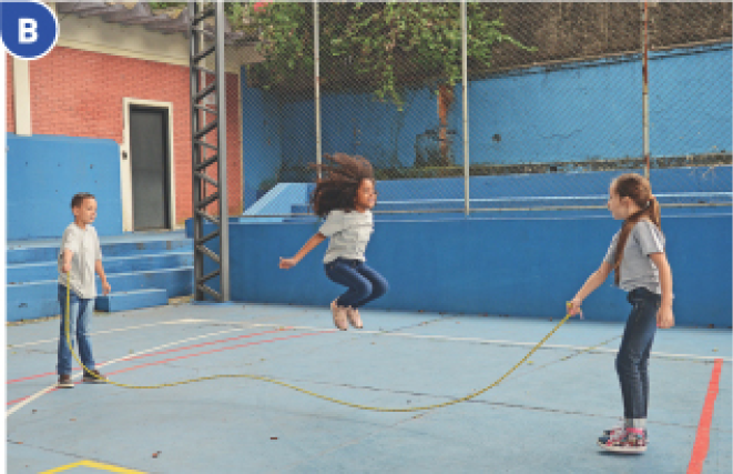 Imagem: Fotografia B. Duas crianças estão girando uma corda e entre elas, uma menina está pulando.  Fim da imagem.