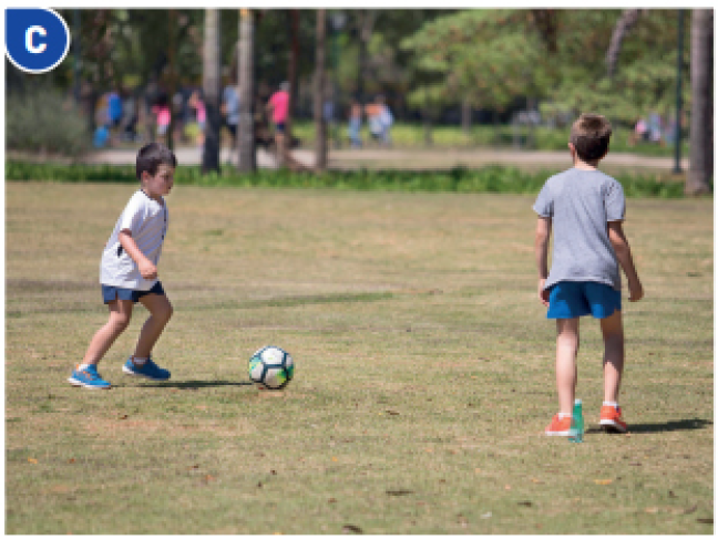 Imagem: Fotografia C. Dois meninos estão correndo atrás de uma bola de futebol. Fim da imagem.