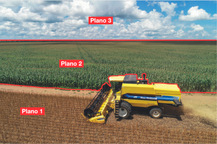 Imagem: Fotografia dividida em planos. Na parte inferior, Plano 1, um trator amarelo está andando sobre uma plantação seca. Em seguida, Plano 2, uma plantação extensa e verde. Na parte superior, Plano 3, nuvens brancas no céu azul. Fim da imagem.