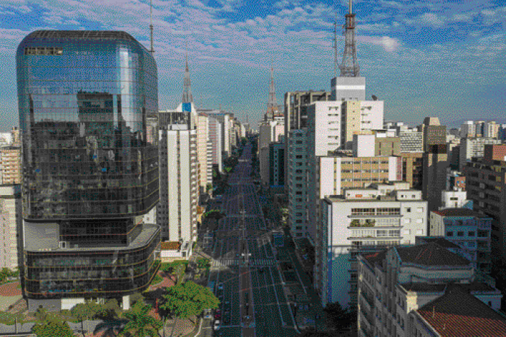 Imagem: Fotografia. Vista aérea de uma avenida. Nas laterais há vários prédios e algumas árvores. Fim da imagem.