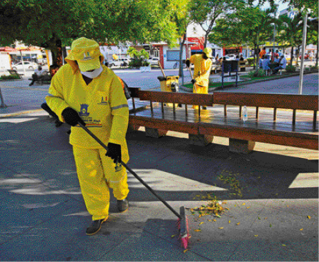 Imagem: Fotografia. Homens com uniforme amarelo estão varrendo uma calçada. Ao fundo, carros e árvores. Fim da imagem.