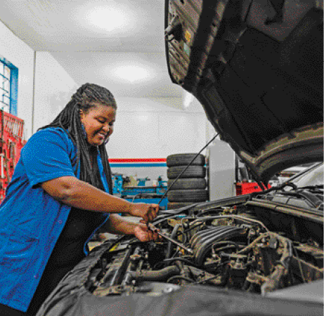 Imagem: Fotografia. Uma mulher com camisa azul está sorrindo e segurando um cabo sobre um capô de carro. Fim da imagem.