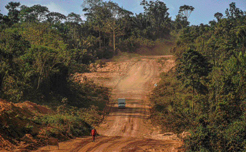 Imagem: Fotografia. Vista aérea de um caminhão sobre uma estrada de terra. Nas laterais há árvores e plantas. Fim da imagem.