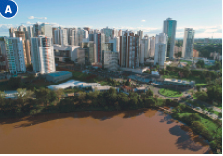 Imagem: Fotografia A. Vista aérea de um lago com água escura. Em volta há árvores, ruas e prédios. Fim da imagem.