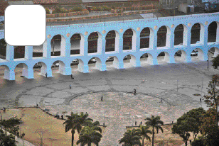 Imagem: Fotografia. Vista aérea de um aqueduto azul e na frente há um pátio extenso e árvores.   Fim da imagem.