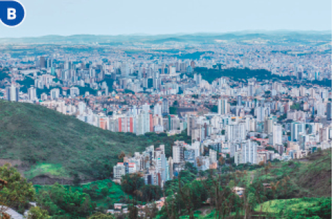 Imagem: Fotografia B. Vista aérea de uma cidade com prédios e construções. Ao lado há morros e árvores.  Fim da imagem.