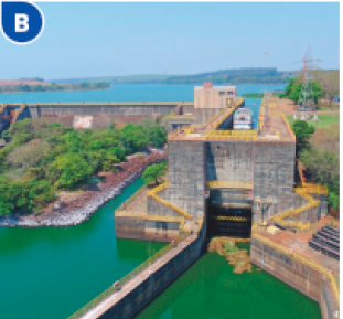 Imagem: Fotografia B. Vista aérea de uma barragem com água em tons de verde.  Fim da imagem.