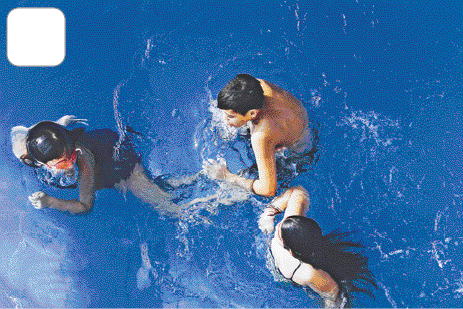 Imagem: Fotografia. Vista de cima de três crianças brincando dentro de uma piscina.  Fim da imagem.