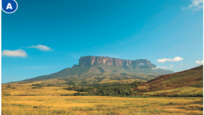 Imagem: Fotografia A. No centro, um campo com grama em tons de verde. Ao fundo, um morro, árvores e o céu azul.  Fim da imagem.