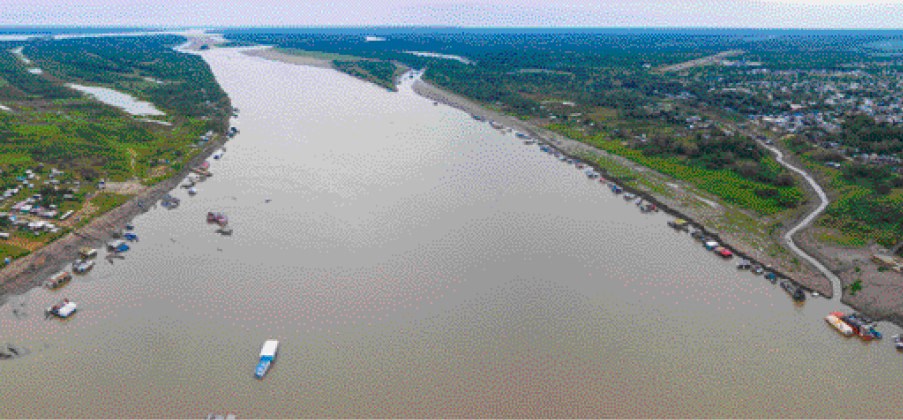 Imagem: Fotografia. Vista aérea de um rio largo com barcos nas margens. Ao lado há casas e árvores.  Fim da imagem.