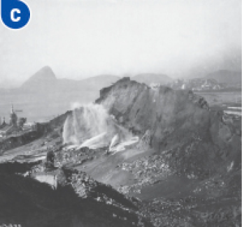 Imagem: Fotografia C em preto e branco. Vista aérea de um morro sendo demolido.   Fim da imagem.