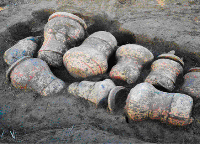 Imagem: Fotografia. Urnas sujas de terra e dentro de um buraco.  Fim da imagem.