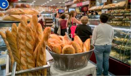 Imagem: Fotografia C. Pessoas em fila e em volta delas há vários pães expostos.  Fim da imagem.