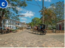 Imagem: Fotografia C. Uma charrete sobre uma rua de pedras. Ao fundo, árvores e construções. Fim da imagem.