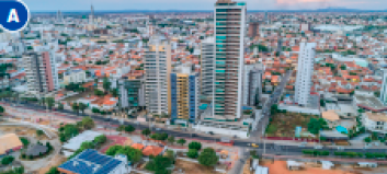 Imagem: Fotografia A. Vista aérea de uma cidade com ruas, prédios, casas e árvores.  Fim da imagem.