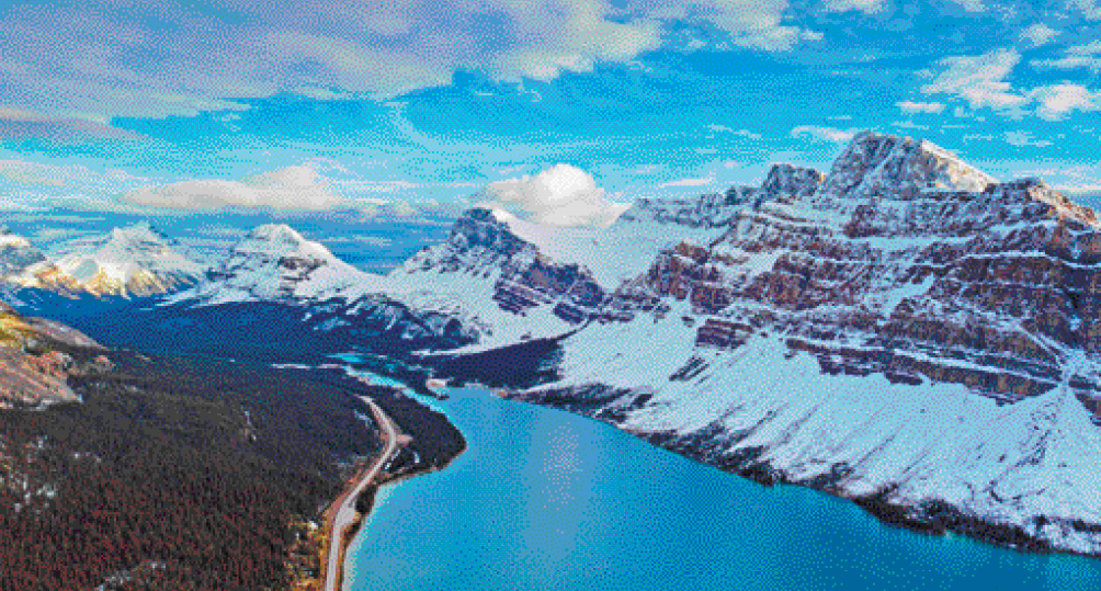 Imagem: Fotografia. Vista aérea de um lago com água azul. À esquerda há morros com vegetação e à direita, montanhas cobertas de neve. Fim da imagem.