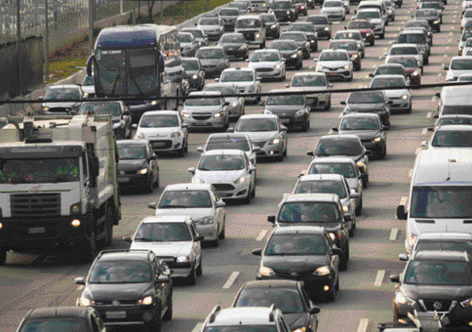 Imagem: Fotografia. Vários automóveis enfileirados em uma avenida.  Fim da imagem.