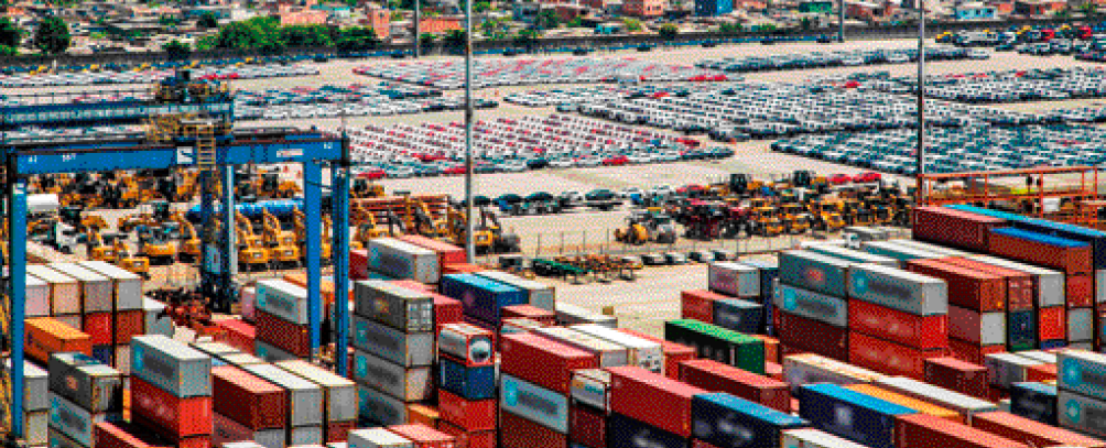 Imagem: Fotografia. Vista aérea de milhares de contêineres empilhados. Ao fundo, vários carros estacionados.   Fim da imagem.