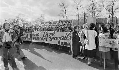 Imagem: 1979 - Convenção sobre a Eliminação de Todas as Formas de Discriminação contra as Mulheres.  Fotografia em preto e branco. Várias mulheres em uma rua, segurando faixas e cartazes.  LEGENDA: Manifestação contra a discriminação de mulheres em Paris, na França, em 1979. FIM DA LEGENDA.   Fim da imagem.