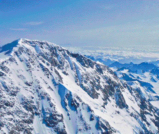 Imagem: Fotografia. Vista aérea de um morro coberto de neve. Ao fundo, mais morros e neve.  Fim da imagem.