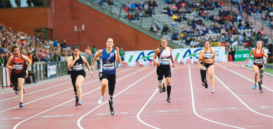 Imagem: Fotografia. Seis mulheres correndo em uma pista. Todas usam um suporte para uma das pernas.  Fim da imagem.