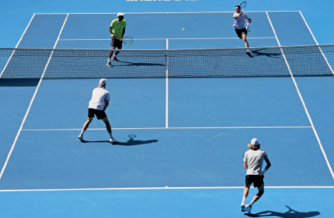 Imagem: Fotografia. Uma quadra azul, com uma rede no meio, com dois jogadores de cada lado segurando raquetes.  Fim da imagem.