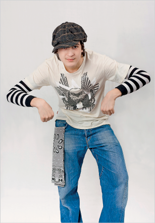 Imagem: Fotografia. Um menino com boina, camisa de manga cumprida e calça jeans. Ele está com os cotovelos flexionados, os braços na altura do tórax e as mãos fechadas  Fim da imagem.